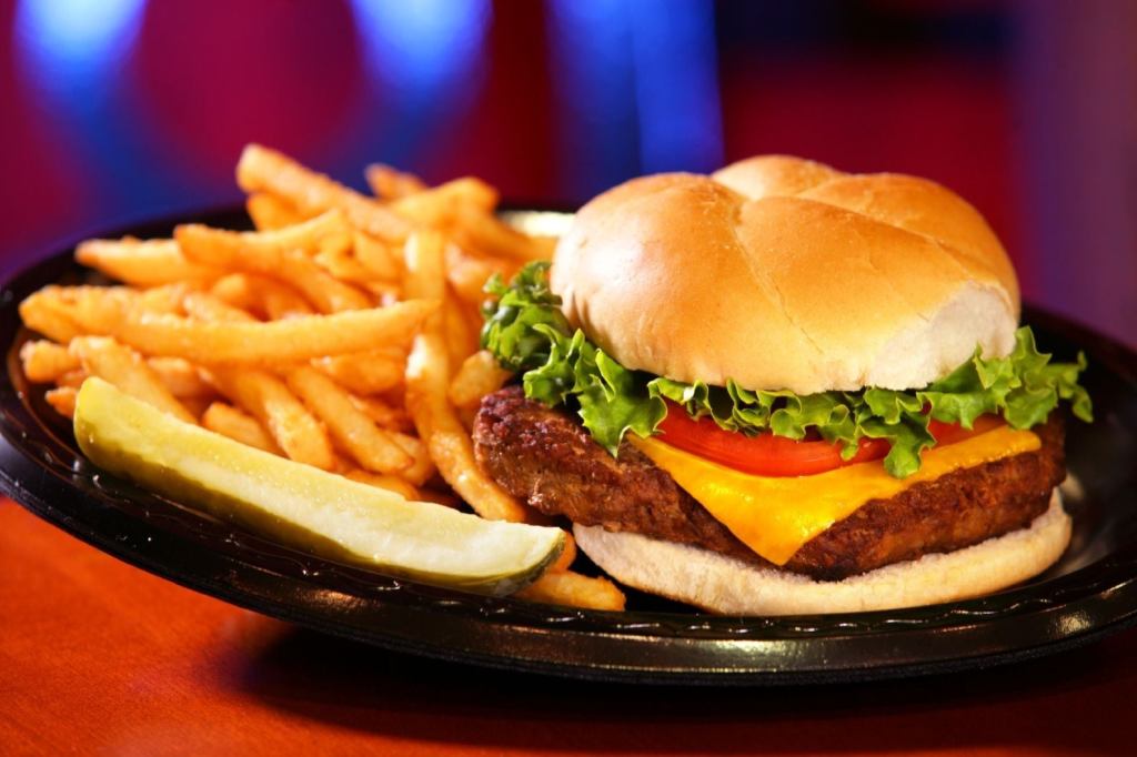 Cheeseburger and fries with a pickle on a black plate